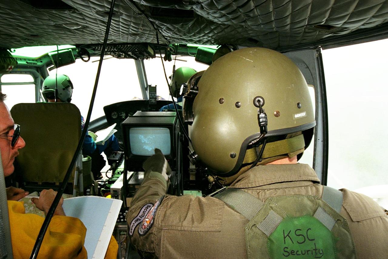 View from the backseat of a NASA Huey UH-1 helicopter showing a KSC Security Services employee pointing at a screen.