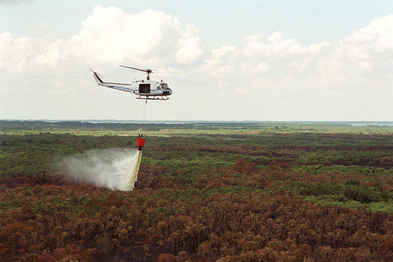 A helicopter dumps a large bucket of water on a forest