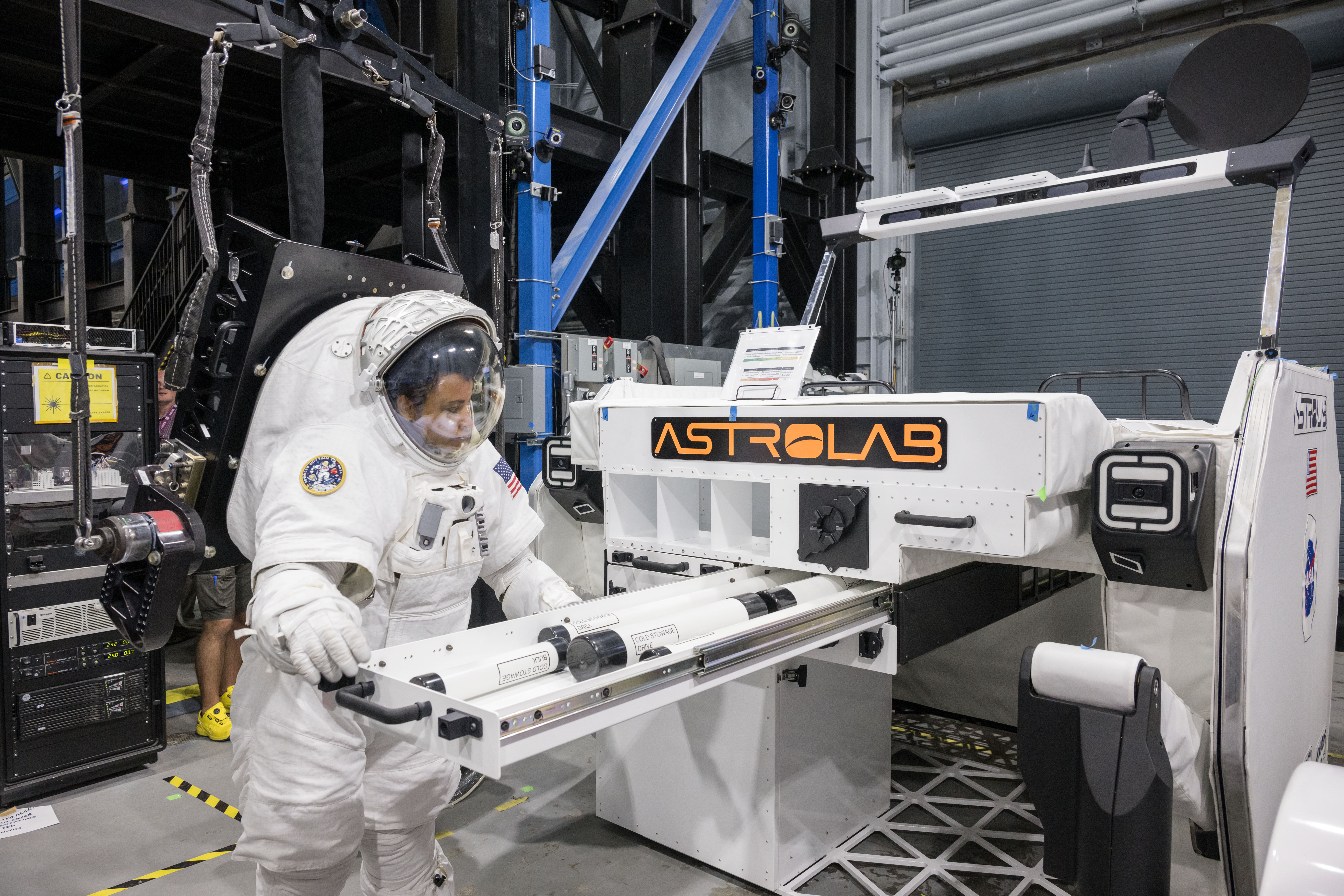 NASA astronaut Jessica Watkins is wearing a white spacesuit while she puts science payloads in a stowage drawer outside of Astrolab's white lunar t...